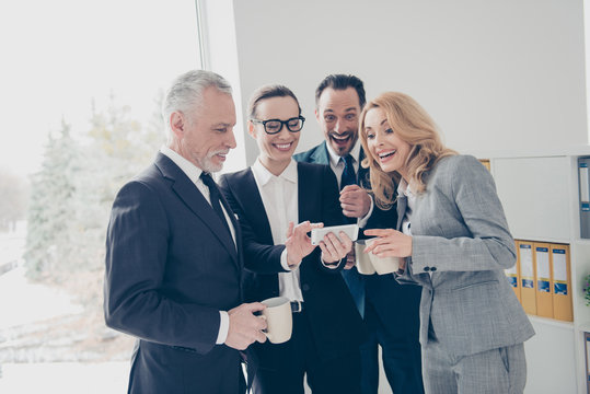 Portrait of four attractive, cheerful, stylish business persons using smart phone, watching funny, comic video, photo, drinking coffe, tea, enjoying leisure, standing in work place, station