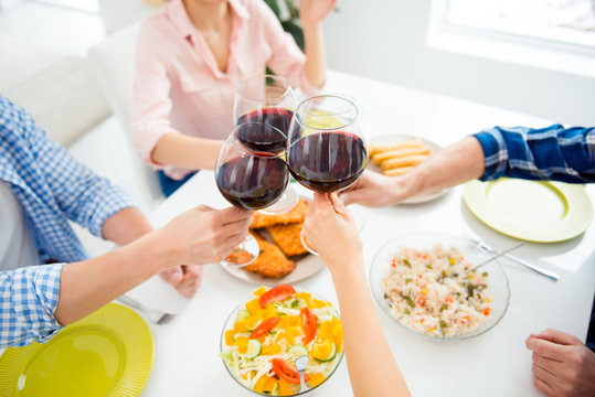 Cropped portrait of people's hands clinking glasses of red wine sitting at the table with appetizing dishes, having dinner, supper together, drinking, sharing alcohol