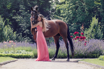 Reiterin lehnt sich im Wind an ihr Pferd in einem Park voller Blumen
