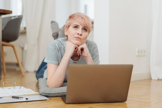 Thoughtful woman working with laptop on floor