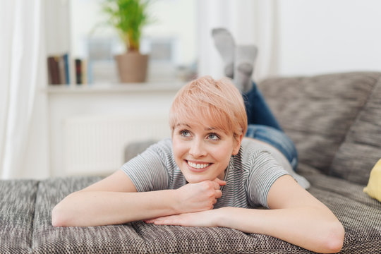 Happy young woman relaxing daydreaming on a sofa