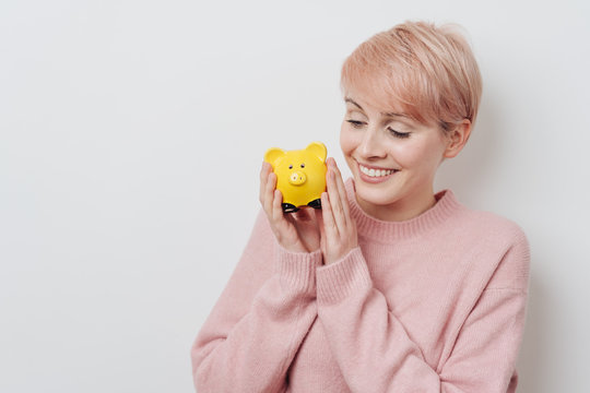 Young woman holding a bright yellow piggy bank