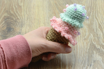 hand holding crochet ice cream cone made of wool on table background.