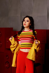 Studio fashion shooting. The girl in a bright outfit, top and pants flared in red and orange colors. Brunette with curly hair . Keeps your braids with your hands