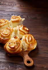 Homemade rose buns on wooden cutting board over rustic vintage background, close-up, shallow depth of field