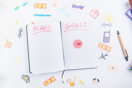 Top view pushpin as an arrow on target icon in personal planning organizer with Goals and Plans among other icons of actions on the working place. Concept of planning and goals achievements.