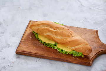 Fresh and tasty sandwich with cheese and vegetables on cutting board over white textured background, selective focus.