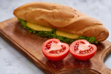 Fresh and tasty sandwich with cheese and vegetables on cutting board over white textured background, selective focus.