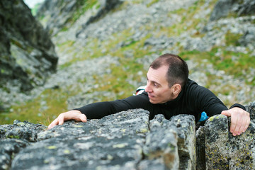 Young man makes hard climbing a steep rock without rope.