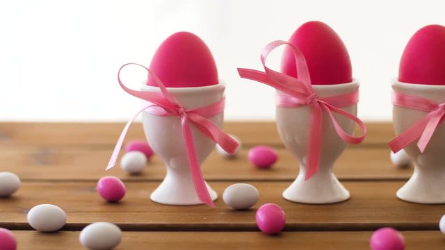 easter, food and holidays concept - pink colored eggs in ceramic cup holders and drop candies on table