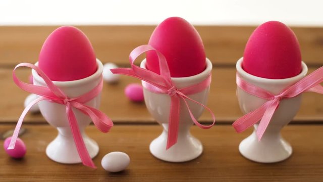 easter, food and holidays concept - pink colored eggs in ceramic cup holders and drop candies on table
