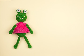 toy frog in a dress, crocheted, on a gentle yellow background..