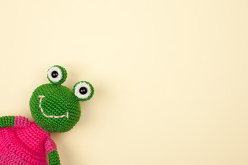 toy frog in a dress, crocheted, on a gentle yellow background..