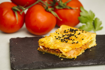 Meat pie on a plate with tomatoes in the background.