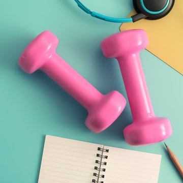 Pastel styled stock photography of fitness equipment dumbbells notepad pencil and earphone on color background. Flat lay.