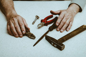 Table composition with tools (nippers, hammer, pliers, rasp, bolt) and hands of elderly working man.