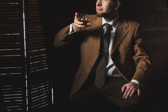 Man in suit with cognac glass in luxury interior. No face