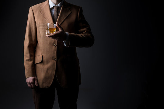 Man in suit with whiskey glass on dark background. No face