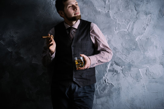 Man in vest standing, leaning against the wall, holding a glass of whiskey (highball)