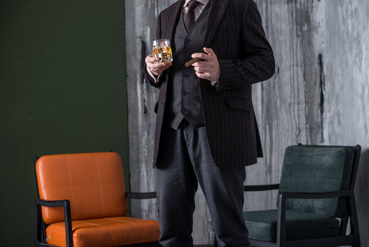 Man in expensive suit is holding whiskey glass in luxury interior. No face