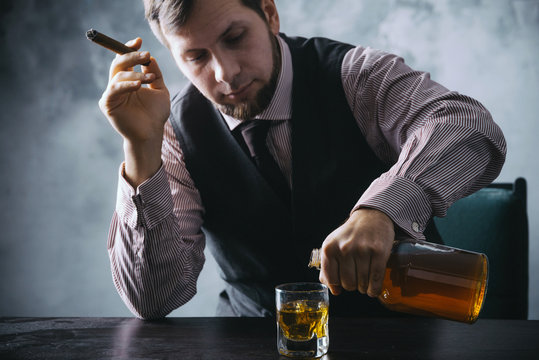 A man sits at a table and pours into a glass from a bottle of whiskey