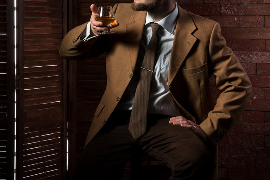 Man in suit with cognac glass in luxury interior. No face