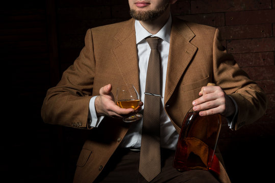 Man in suit with cognac glass and bottle in luxury interior. without face