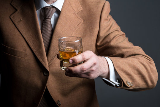 Handsome bearded businessman is drinking expensive whisky closeup. No face
