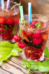 Glasses of refreshing drink flavored with fresh fruit and decorated with cherries covered with dew drops