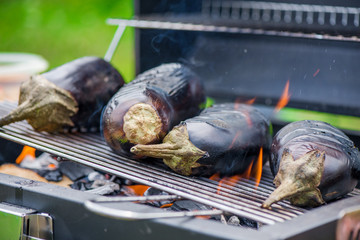 Aubergine on barbecue grill on hot charcoal and fire. Preparing healthy food on holiday. Cooking vegetables on flames. Delicious meal for vegetarians and vegans 