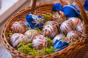 Easter eggs prepared for dyeing in onions peels, decorated with natural fresh leaves, plants, rice, colorful fabric and tied with white threads. Eggs laying in wicker wooden basket full of green grass
