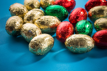 mehrere Schokoladeneier in bunter Ostereier Folie Gelb Gold Grün Rot blauer Hintergrund