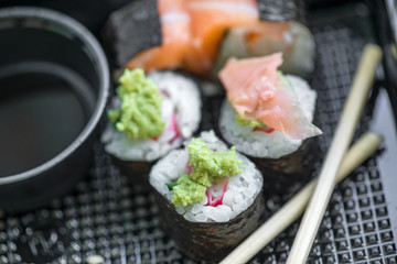 Fresh and delicious maki and nigiri sushi rolls with tiger shrimps, salmon, philadelphia cheese and wasabi served with soy sauce and ginger slices on black take away plate. Japanese food in restaurant