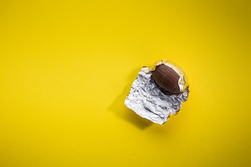 Schokoladenei in bunter Osterei Folie gelber Hintergrund