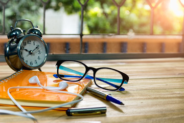 A desk in the morning with a notebook for notes, glasses, alarm clocks and headphones.