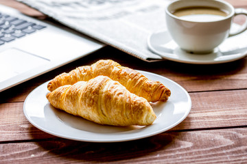 Business lunch with croissant and laptop on wooden desk