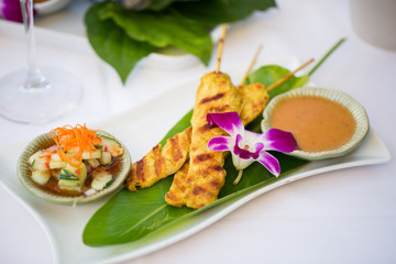 Thai Chicken Satay with Sauce Appetizer on a White Plate with an Orchid