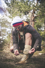 Handsome strong stylish  man tying his shoes in forest outdoor and mountains in the background