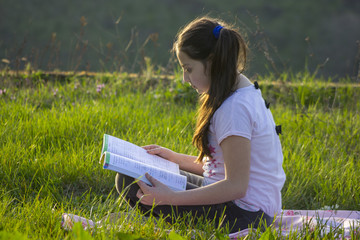 ittle girl reading book on the grass