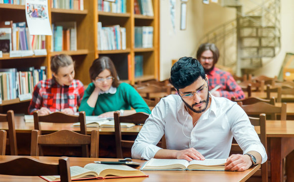 Bearded student man wears white shirt studying with books in the library