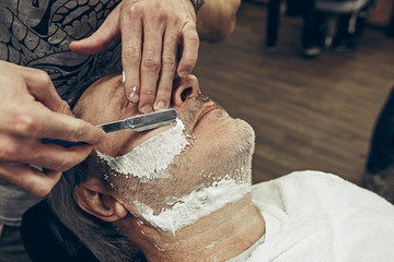 Close-up side top view handsome senior bearded caucasian man getting beard grooming in modern barbershop.