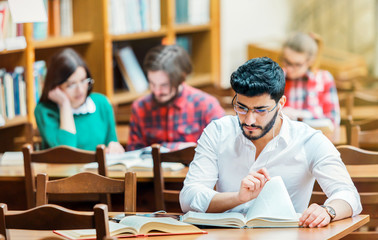 Portrait of successful bearded student man wears white shirt studying with books in the library