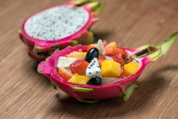 Fruit salad in dragonfruit on wood background