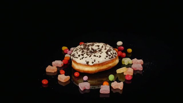 white funny surprised glazed donut with sprinkles, striped caramel candies, colorful dragee with raisins or peanuts inside rotate on black background