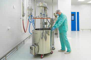 Pharmaceutical factory man worker in protective clothing working with control panel in sterile working conditions