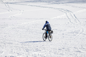 Man riding a bicycle in winter on the snow-covered ice of the Ural River. Photo taken in Russia, in the city of Orenburg