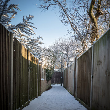 Alley Way With Wooden Fences And Trees Covered In Snow