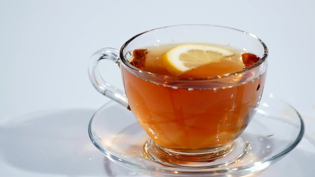 In a cup on a saucer with black tea falls a slice of lemon on a white background, slow mo