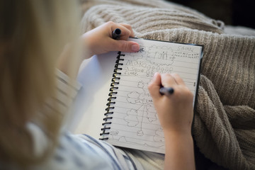 High angle view of girl writing in diary while sitting at home