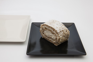 Walnut roll with whipped cream on a black plate.